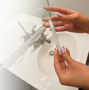 Hands holding the PearliPen whitening pen at a bathroom sink