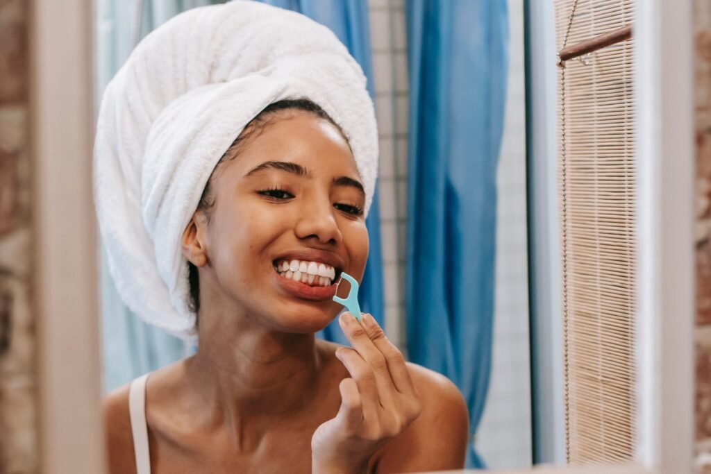 Woman with a towel on her head flossing her teeth in the bathroom mirror