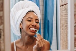 Woman with a towel on her head flossing her teeth in the bathroom mirror