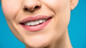 Close-up of a person's lower face with a natural smile against a teal background
