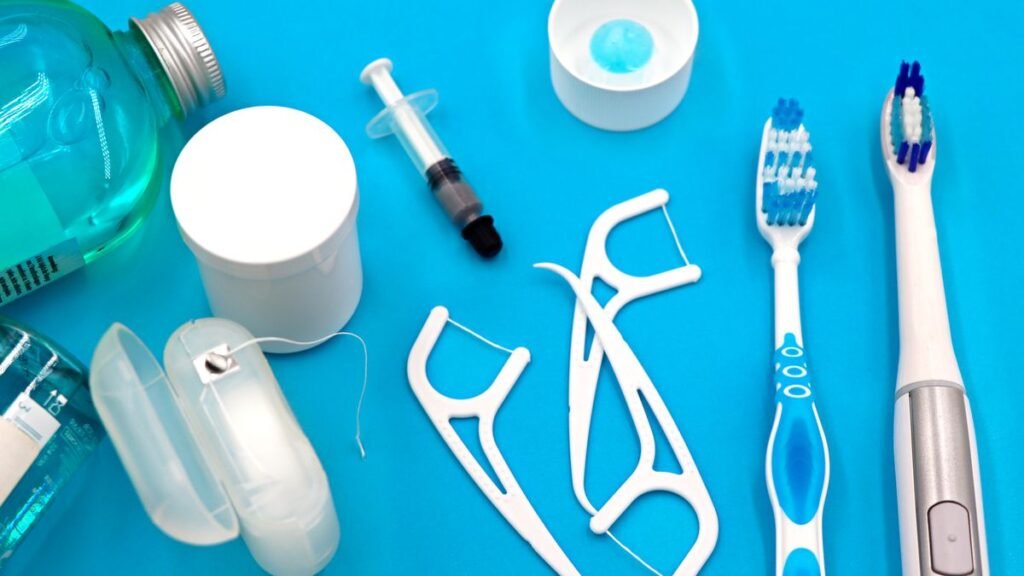 Flat lay of oral hygiene tools including mouthwash, floss, floss picks and toothbrushes on a blue background