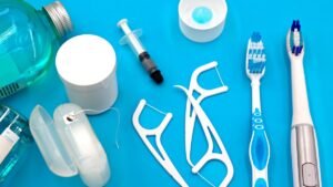 Flat lay of oral hygiene tools including mouthwash, floss, floss picks and toothbrushes on a blue background