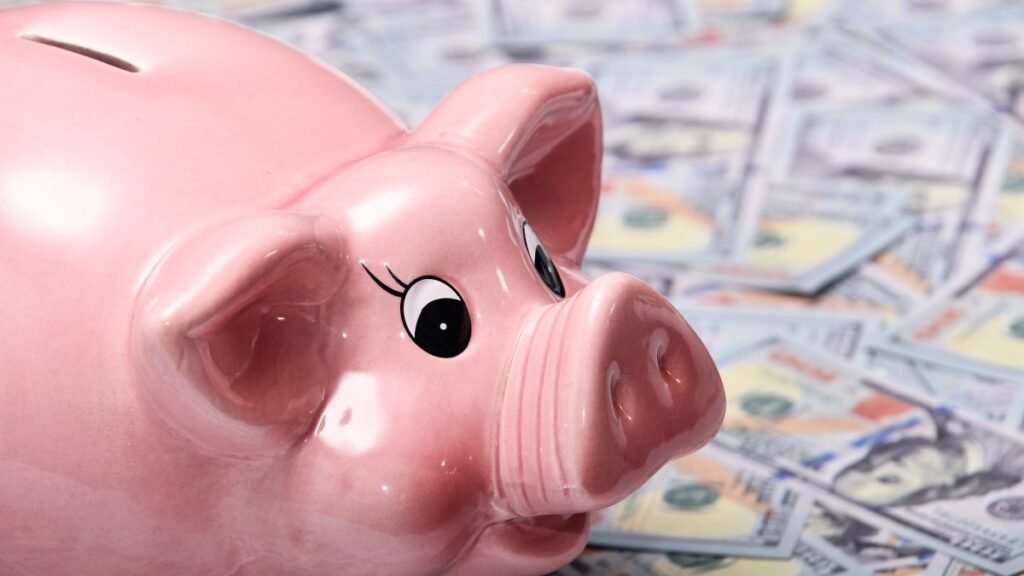 Pink piggy bank resting on a spread of hundred dollar bills