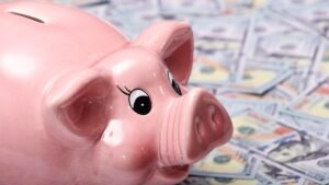 Pink piggy bank resting on a spread of hundred dollar bills
