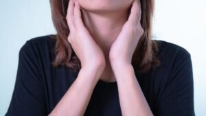 Person in a black shirt holding both hands to their throat